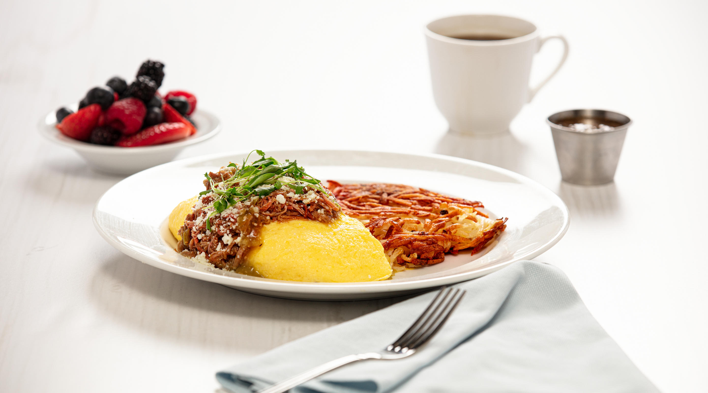 A carnitas omelet with a cup of fruit and coffee.